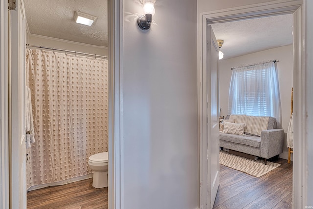 full bath with a shower with shower curtain, a textured ceiling, toilet, and wood finished floors