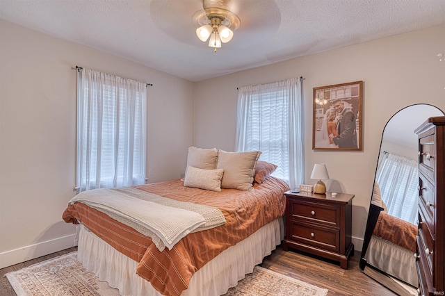 bedroom featuring light wood-style floors, a ceiling fan, baseboards, and a textured ceiling