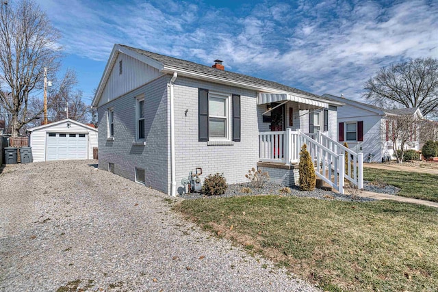 view of front of home featuring brick siding, a detached garage, an outdoor structure, driveway, and a front lawn