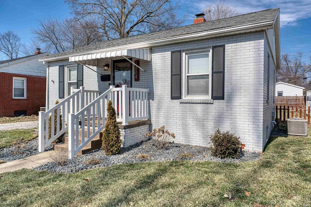 bungalow-style house featuring brick siding, a chimney, a front yard, and cooling unit