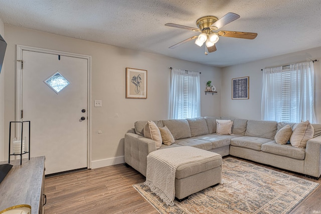 living room with a textured ceiling, ceiling fan, light wood-type flooring, and baseboards