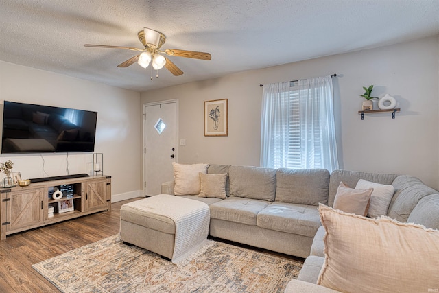 living room with a textured ceiling, dark wood finished floors, a ceiling fan, and baseboards