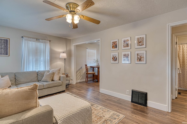 living room featuring baseboards, a textured ceiling, visible vents, and wood finished floors