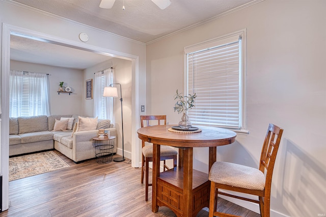 dining room featuring light wood finished floors, a ceiling fan, ornamental molding, a textured ceiling, and baseboards