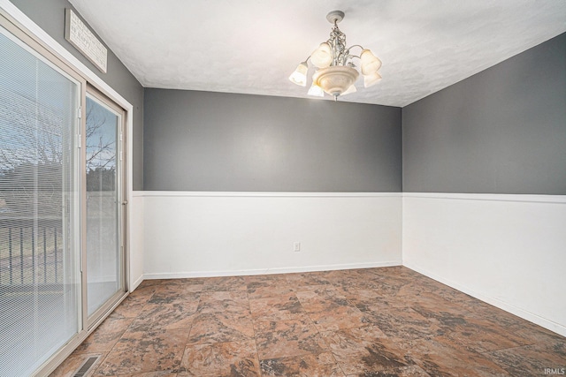 spare room with baseboards, stone finish floor, visible vents, and an inviting chandelier