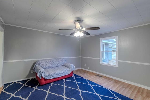 sitting room with a ceiling fan, crown molding, baseboards, and wood finished floors