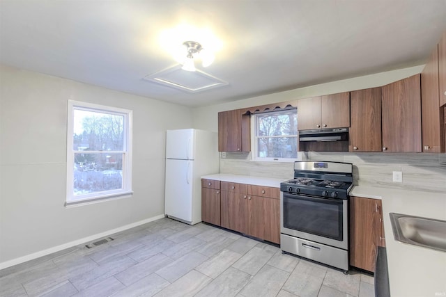 kitchen with gas range, under cabinet range hood, light countertops, and freestanding refrigerator