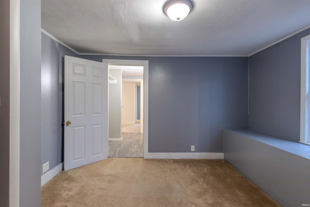 empty room featuring a textured ceiling, carpet, baseboards, and crown molding