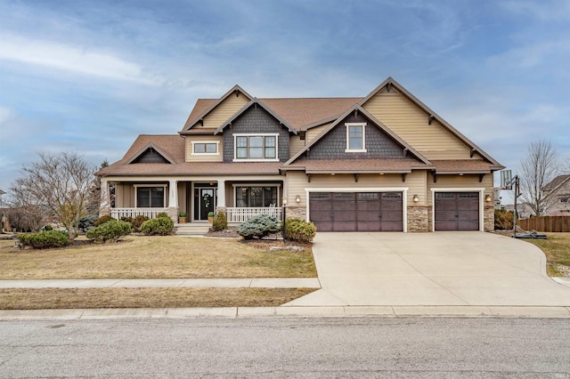 craftsman house featuring covered porch, a garage, driveway, stone siding, and a front lawn