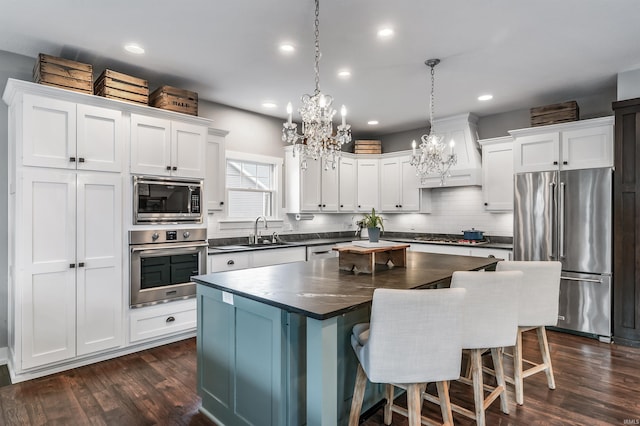 kitchen featuring dark wood-style flooring, dark countertops, appliances with stainless steel finishes, a sink, and a kitchen island