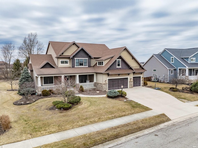 craftsman house featuring a porch, a shingled roof, concrete driveway, stone siding, and a front lawn