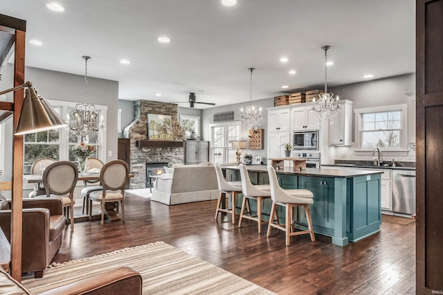 kitchen featuring a stone fireplace, stainless steel appliances, white cabinets, dark wood-style floors, and dark countertops