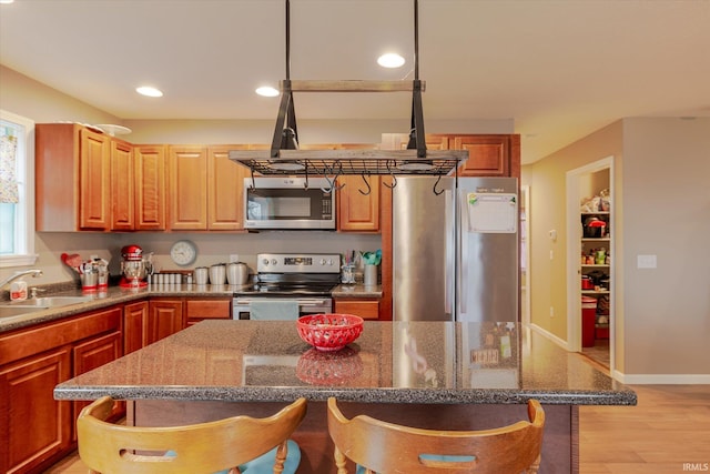 kitchen with a breakfast bar area, stainless steel appliances, a sink, a kitchen island, and light wood-type flooring