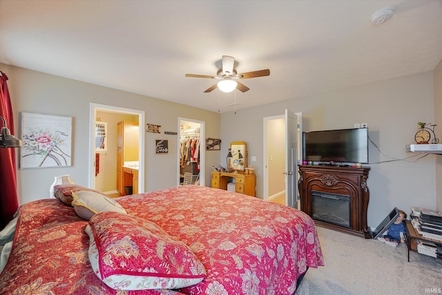 carpeted bedroom featuring a glass covered fireplace, ensuite bath, ceiling fan, a walk in closet, and a closet