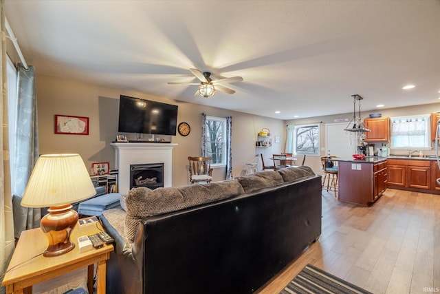 living area with light wood-style floors, recessed lighting, a fireplace, and a ceiling fan