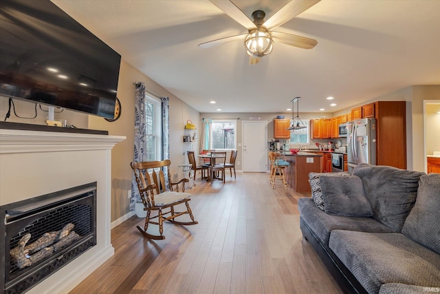 living room with a ceiling fan, a fireplace, light wood-style flooring, and baseboards