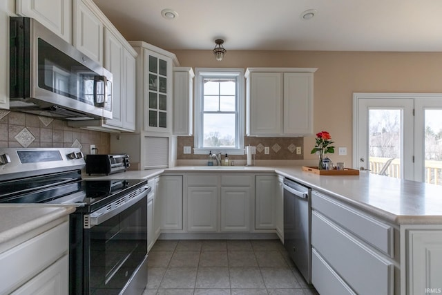 kitchen featuring appliances with stainless steel finishes, a peninsula, a sink, light countertops, and backsplash