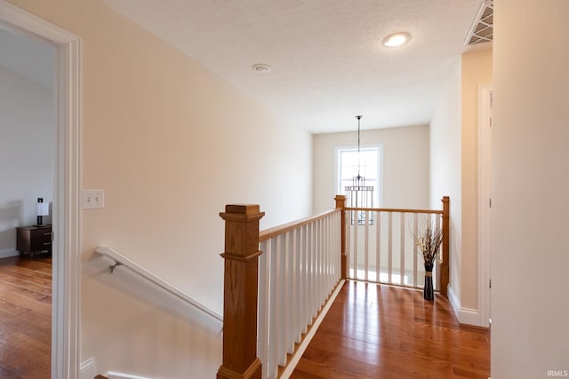 corridor featuring a notable chandelier, visible vents, wood finished floors, and an upstairs landing