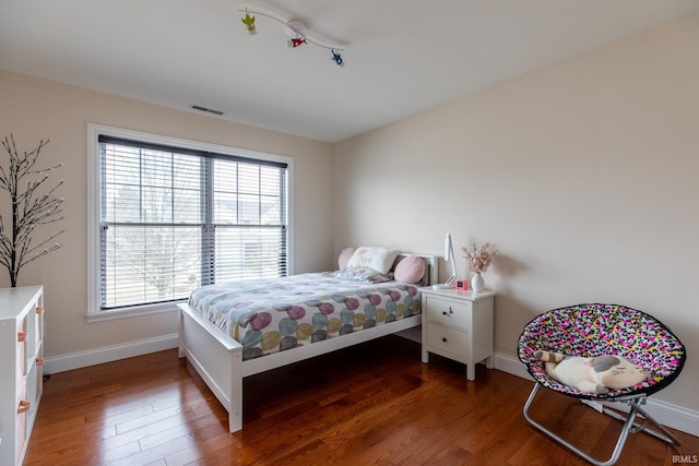 bedroom with baseboards, visible vents, and wood finished floors