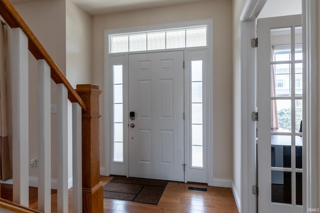 entryway with stairs, wood finished floors, visible vents, and baseboards