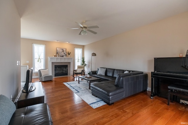 living area with light wood-style floors, a fireplace with flush hearth, baseboards, and ceiling fan