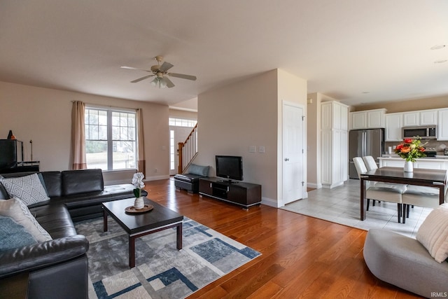 living area featuring ceiling fan, stairway, light wood-type flooring, and baseboards