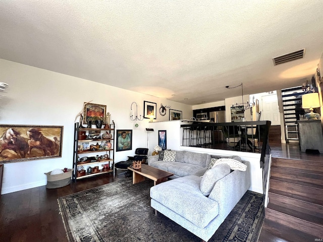 living area with a textured ceiling, wood finished floors, visible vents, and baseboards