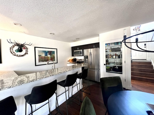 kitchen with dark wood-style flooring, appliances with stainless steel finishes, a textured ceiling, light stone countertops, and a kitchen bar