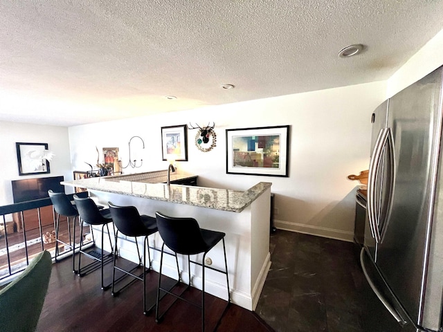 kitchen featuring dark wood-type flooring, freestanding refrigerator, a kitchen breakfast bar, light stone countertops, and baseboards