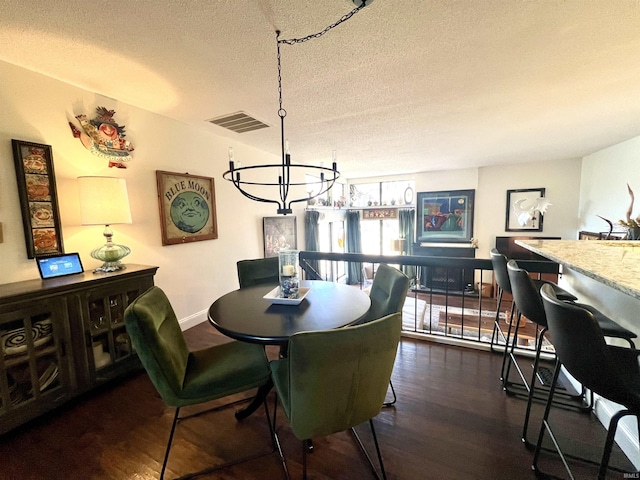 dining area featuring dark wood finished floors, a notable chandelier, visible vents, a textured ceiling, and baseboards