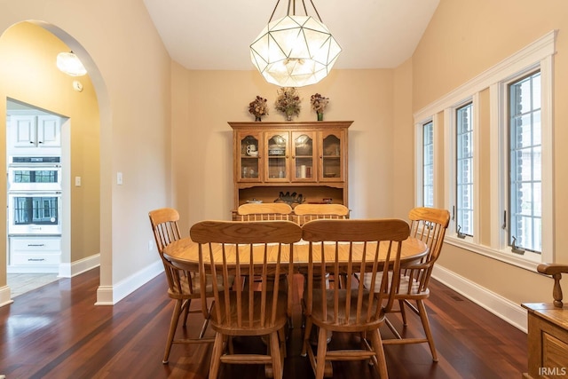 dining room featuring dark wood-type flooring, arched walkways, and baseboards