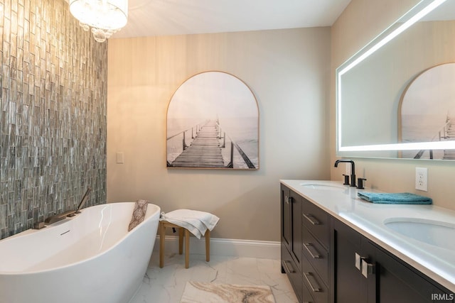 bathroom featuring marble finish floor, double vanity, a freestanding bath, a sink, and baseboards