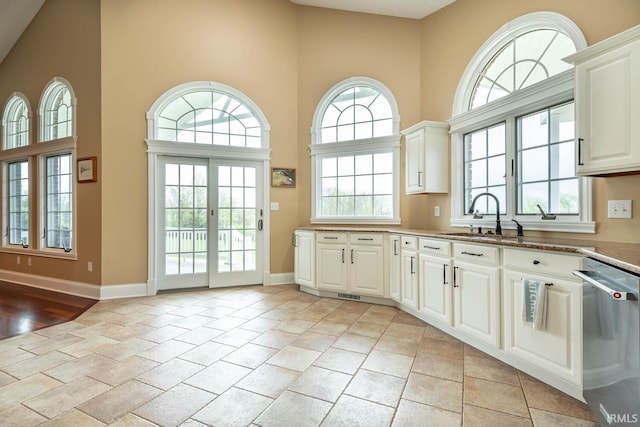 kitchen with a high ceiling, a sink, baseboards, stainless steel dishwasher, and a wealth of natural light