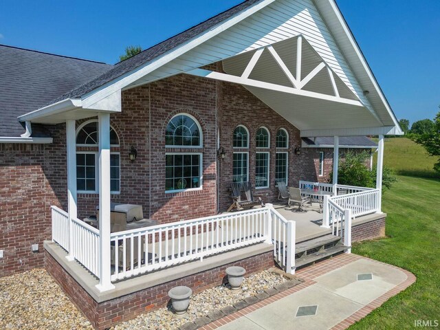 exterior space featuring roof with shingles, brick siding, a lawn, and a porch