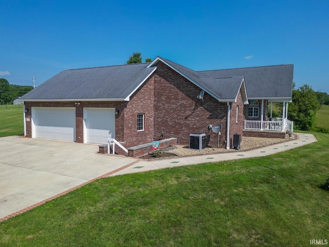 view of side of home with brick siding, central air condition unit, covered porch, a lawn, and an attached garage