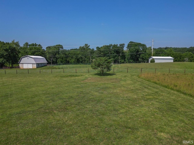 view of yard with a pole building, a rural view, an outdoor structure, and fence