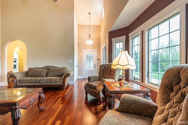 living room featuring arched walkways, dark wood-type flooring, a high ceiling, and a wealth of natural light