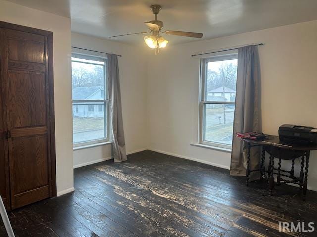 interior space with a ceiling fan, baseboards, and dark wood-type flooring