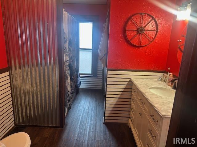 bathroom with a textured wall, toilet, a wainscoted wall, wood finished floors, and vanity