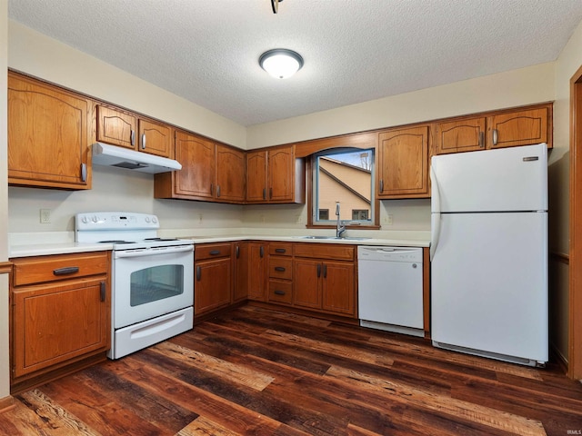 kitchen with brown cabinets, dark wood finished floors, a sink, white appliances, and under cabinet range hood