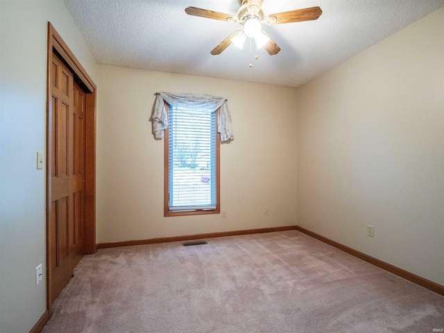 unfurnished room featuring light colored carpet, visible vents, a ceiling fan, a textured ceiling, and baseboards