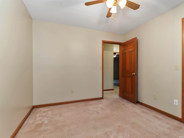 spare room featuring light carpet, ceiling fan, a textured ceiling, and baseboards