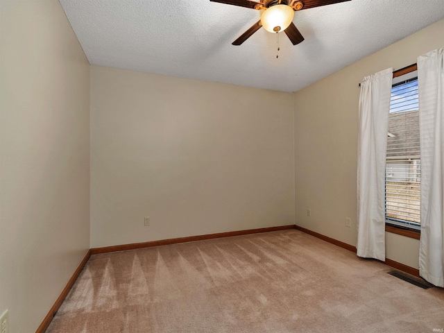 spare room with ceiling fan, a textured ceiling, light carpet, visible vents, and baseboards