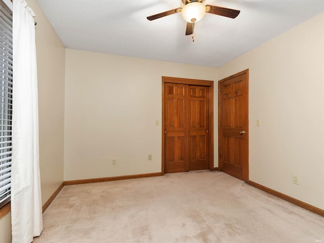 unfurnished bedroom featuring light carpet, a textured ceiling, a ceiling fan, and baseboards