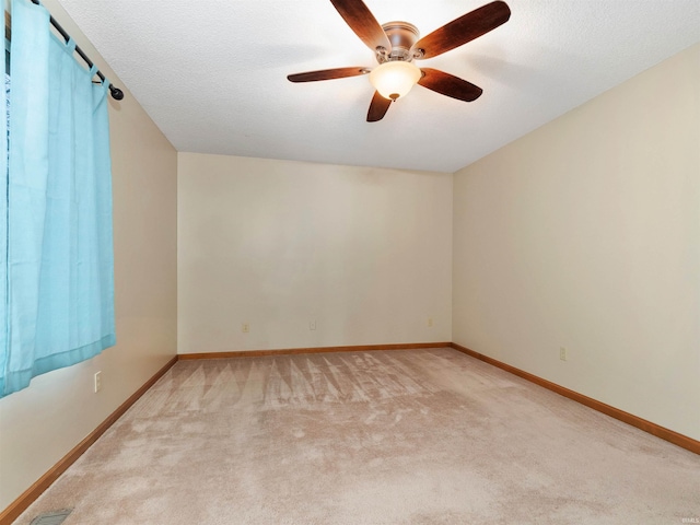 spare room featuring light carpet, a ceiling fan, baseboards, and a textured ceiling