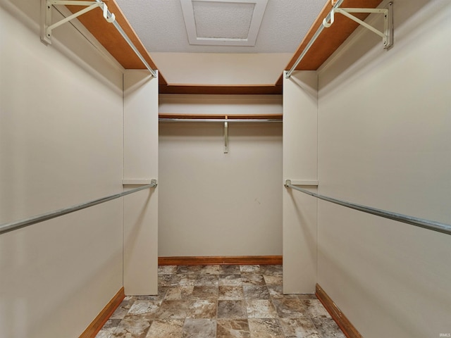 walk in closet featuring attic access and stone finish floor