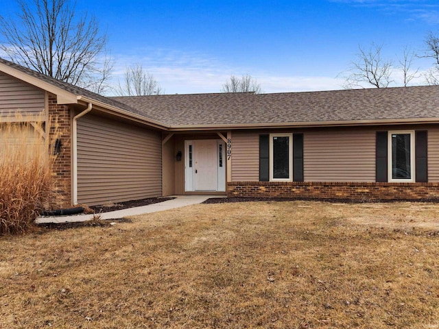 doorway to property featuring a shingled roof, brick siding, a yard, and an attached garage