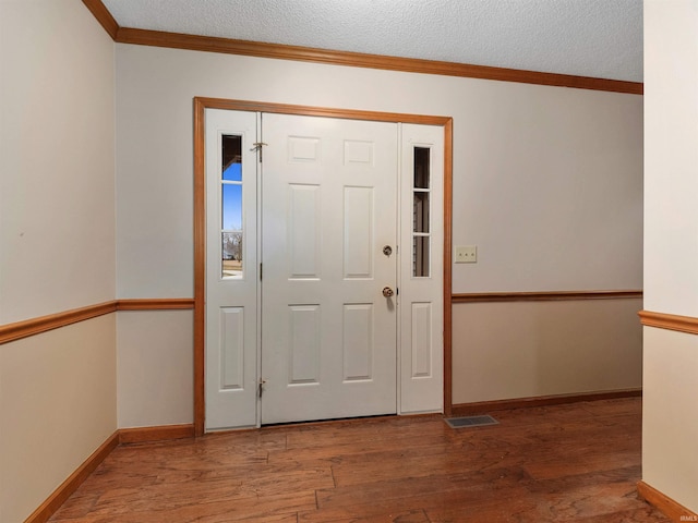 entrance foyer featuring visible vents, ornamental molding, a textured ceiling, wood finished floors, and baseboards