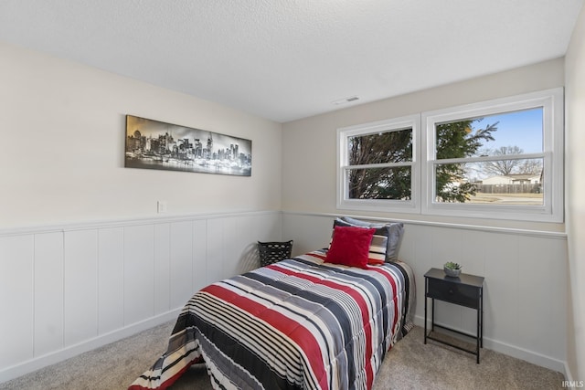 carpeted bedroom featuring a textured ceiling, a wainscoted wall, and visible vents