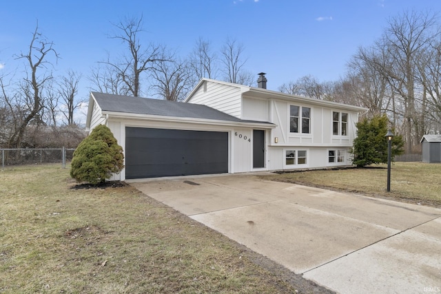 split level home with a chimney, concrete driveway, fence, a garage, and a front lawn